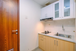Une cuisine de taille réduite avec des meubles blancs, un évier en acier inoxydable et une porte en bois.