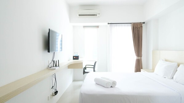 A hotel room with a bed, a desk, a chair, a television, and a window with curtains.