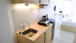A compact kitchenette with a sink, a coffee maker, and a compact stove. - Good Studio Connected To Mall At Orchard Supermall Mansion Apartment (Surabaya)