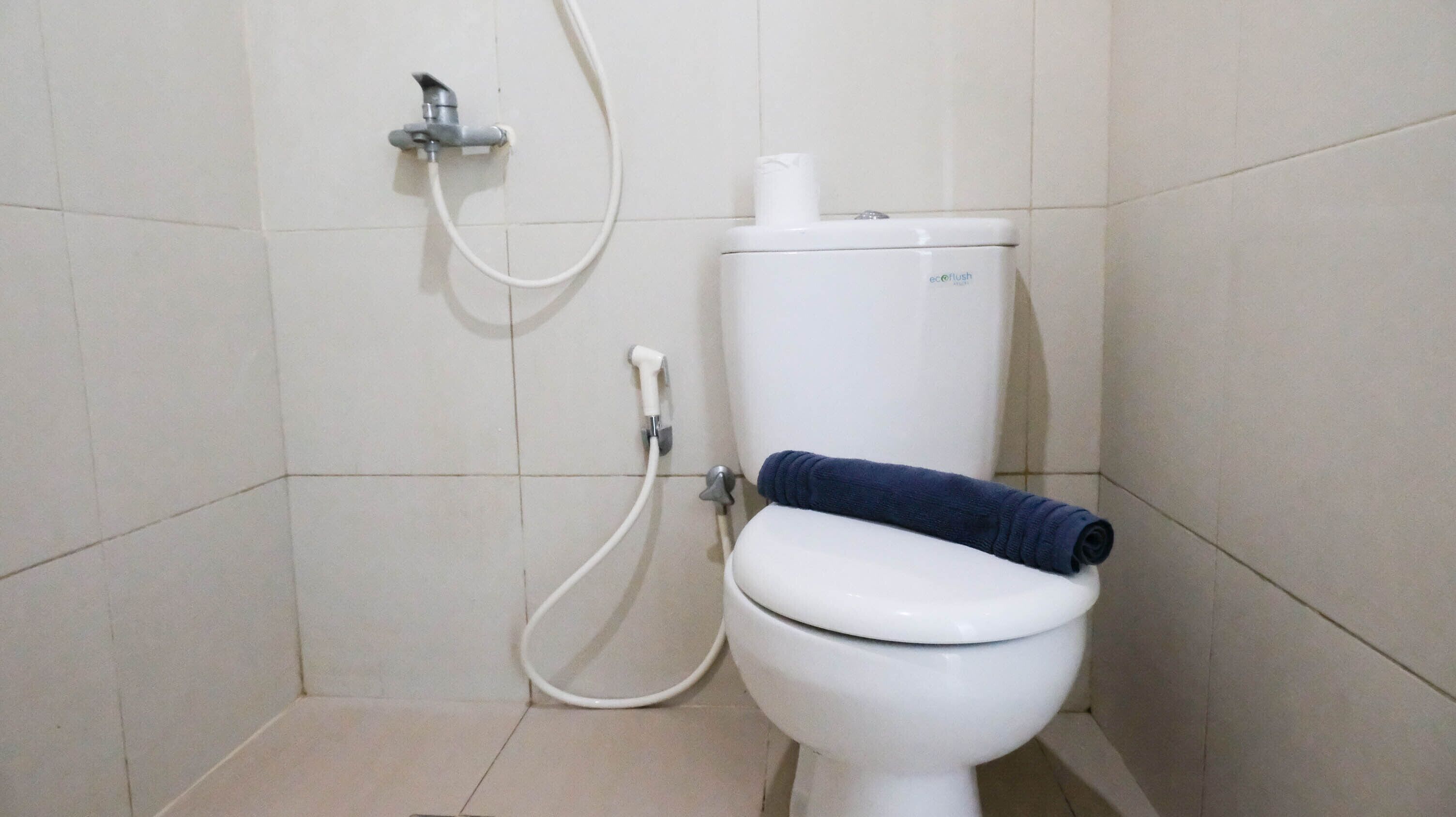 Een wit toilet met een blauwe handdoek op de bril, een witte spoelgreep en een witte spoelknop.