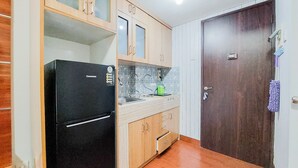 A compact kitchen with wooden cabinets, a black refrigerator, a sink, and a door with a towel hanging on it. - Good And Clean Studio Room Serpong Greenview Apartment (South Tangerang)