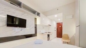 A modern bathroom with a marble wall, a flat-screen TV, a sink, and a wooden bench. - Studio Full Furnished With Comfort Design At Sky House Bsd Apartment (Pagedangan)
