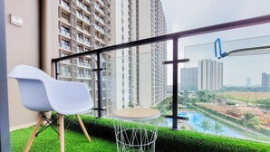 A balcony with a white chair, a small round table, and a view of tall buildings and a river. - Studio Full Furnished With Comfort Design At Sky House Bsd Apartment (Pagedangan)