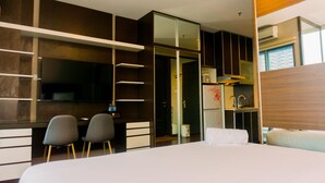 A modern hotel room with a large bed, a desk with two chairs, a wardrobe, and a small kitchenette. - Homey And Minimalist Studio Room At Gp Plaza Apartment (Jakarta)