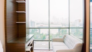 A modern living room with a glass partition, a white sofa, and a view of a cityscape through large windows. - Homey And Minimalist Studio Room At Gp Plaza Apartment (Jakarta)