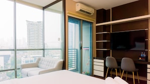 A hotel room with a large bed, a sofa, two chairs, a TV, and a view of the city. - Homey And Minimalist Studio Room At Gp Plaza Apartment (Jakarta)