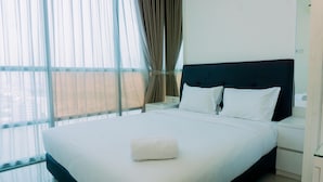 Een hotelkamer met een groot bed, witte lakens, een zwart hoofdeinde en uitzicht door dunne gordijnen.