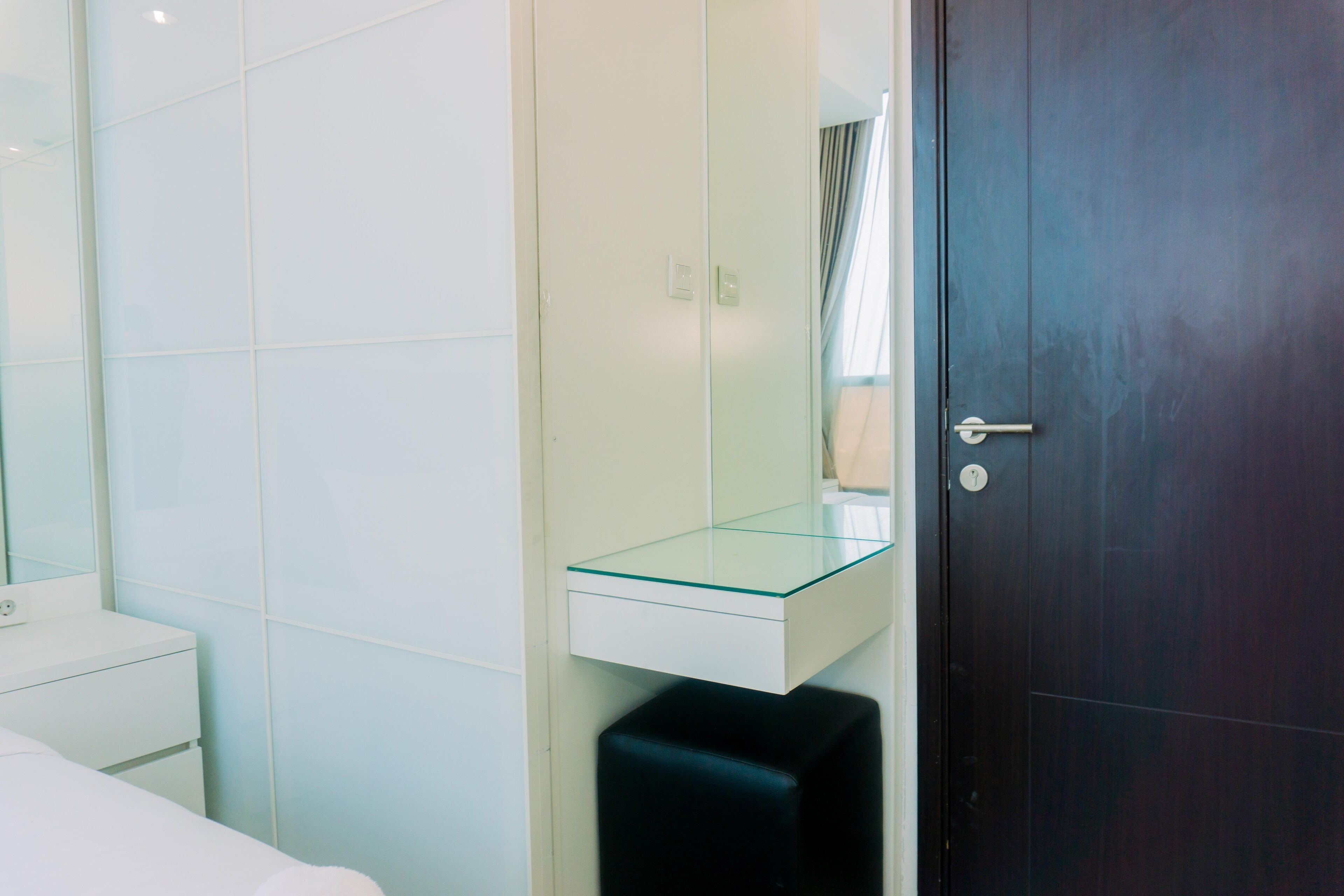 Un baño moderno con repisa de vidrio, inodoro blanco y puerta de madera oscura.