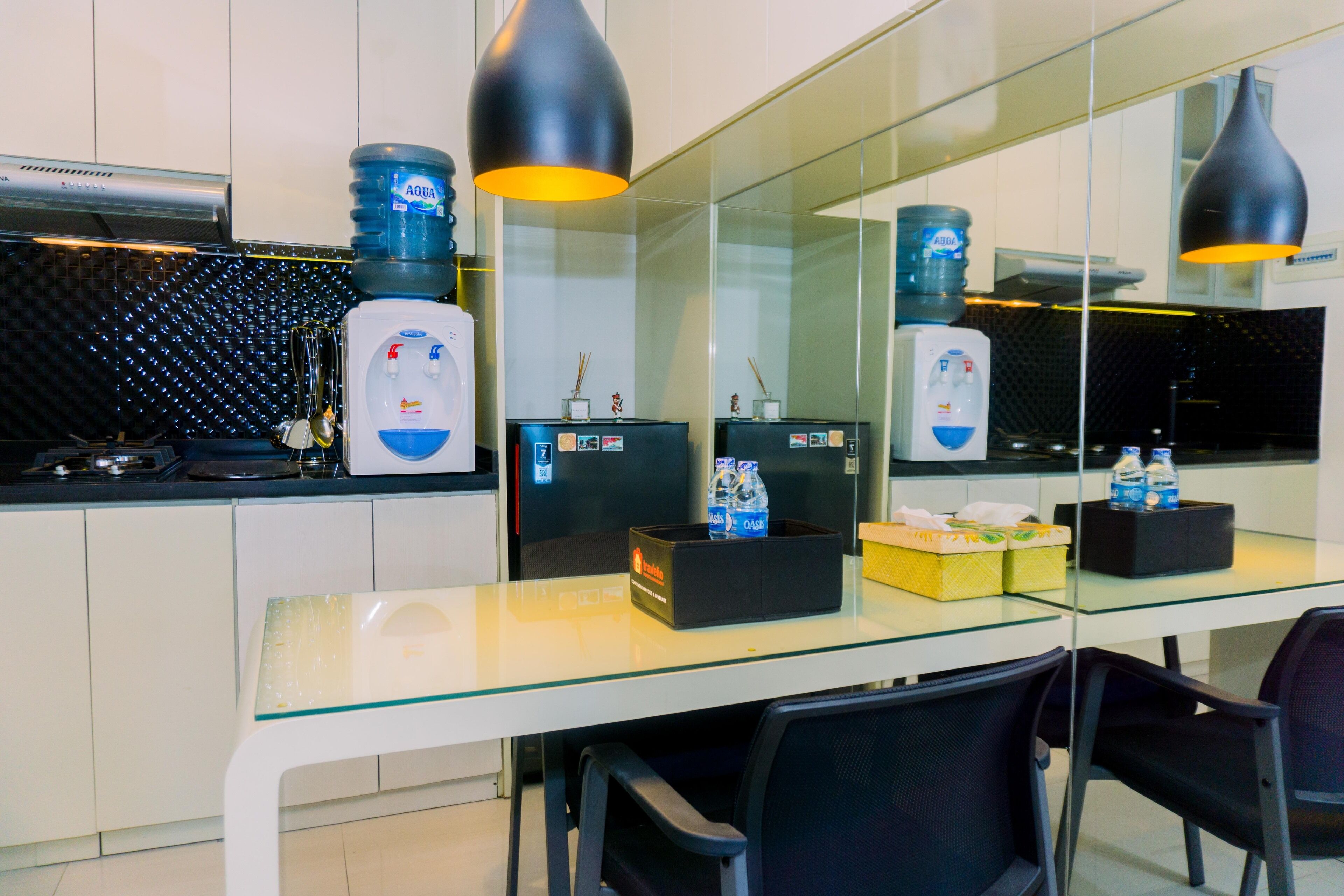 A modern kitchen with a glass dining table, black chairs, and water dispensers.