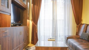 Ein Wohnzimmer mit einer Ledersofa, Holzschränken, einem Glastisch und einem großen Fenster mit Vorhängen.
