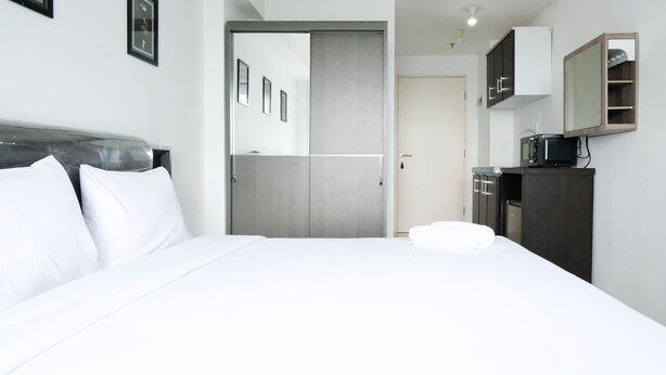 A hotel room with a bed, a wardrobe, a mirror, and a small kitchenette. - Comfy And Modern Studio (No Kitchen) At Orchard Supermall Mansion Apartment (Surabaya)