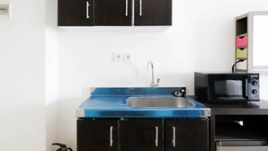 A compact kitchen with a blue countertop, a stainless steel sink, and a black microwave. - Comfy And Modern Studio (No Kitchen) At Orchard Supermall Mansion Apartment (Surabaya)