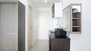A compact kitchen with a built-in microwave, a sink, and a wooden cabinet. - Comfy And Modern Studio (No Kitchen) At Orchard Supermall Mansion Apartment (Surabaya)