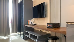 Ein modernes Hotelzimmer mit einem Holztisch, zwei schwarzen Barhocker, einem flachbildfernseher an der Wand, einem kleinen runden Spiegel und einer Reisetasche mit dem Aufdruck 'Travelio'.