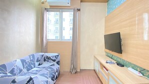 A room with a bed, a TV mounted on the wall, and a window with curtains. - Modest 2Br Apartment At Suites @Metro (Bandung)
