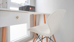 A white chair with wooden legs and a black box labeled "Travelio" on a white desk near a window. - Simply And Cozy Living Studio At Tokyo Riverside Pik 2 Apartment (Teluknaga)
