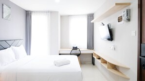 A hotel room with a bed, a desk, a TV, and a shelf with a thermostat and a phone.