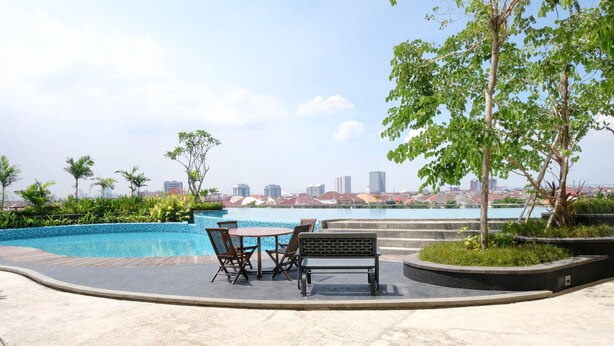 A poolside area with a table and chairs, surrounded by greenery and overlooking a cityscape.
