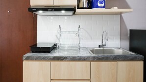A kitchen with a black induction cooktop, a stainless steel sink, wooden cabinets, and a white tiled backsplash.