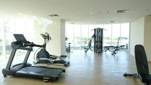 A gym with cardio machines, weight training equipment, and large windows offering a view of the outdoors.