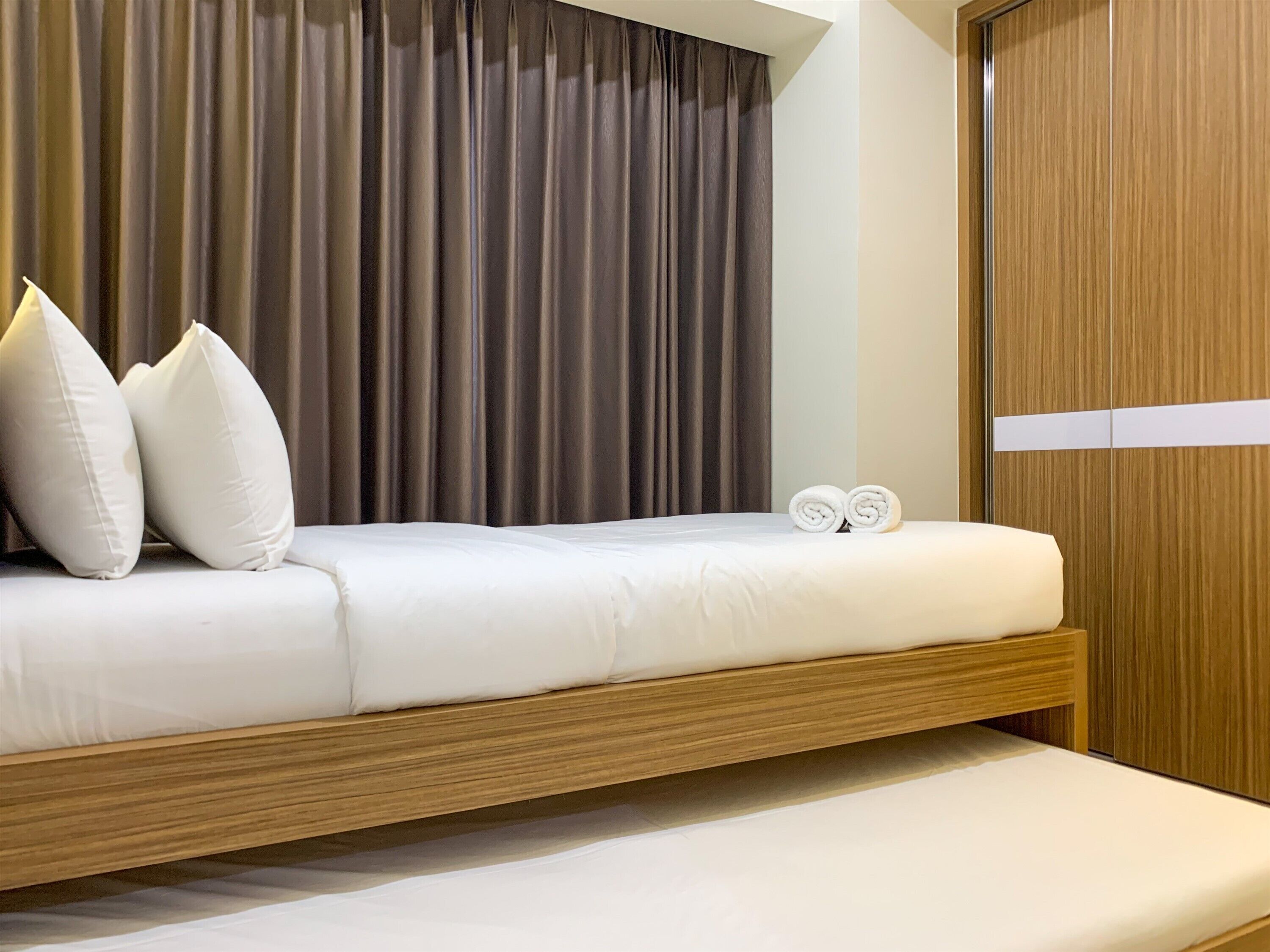 Une chambre d’hôtel moderne avec un cadre de lit en bois, du linge de lit blanc et une grande fenêtre avec des rideaux.