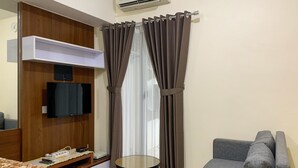 Un salon moderne avec un canapé gris, une petite table ronde, un téléviseur fixé au mur et un meuble en bois.