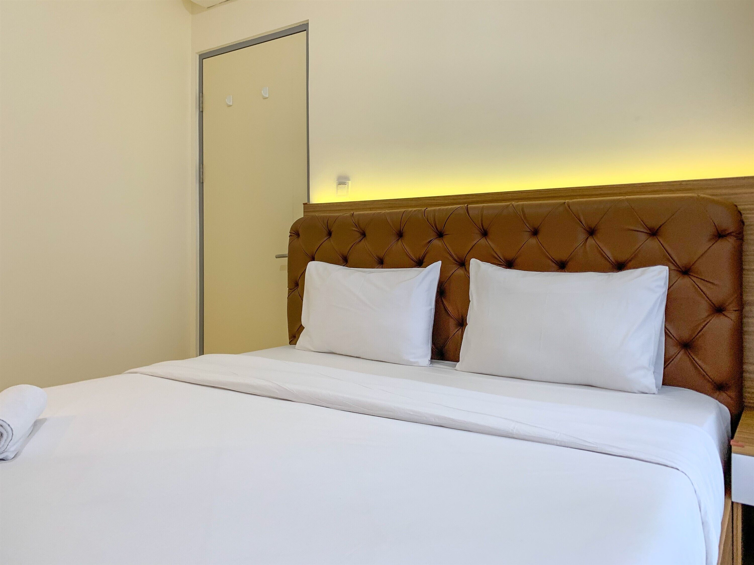A neatly made bed with white linens and a brown tufted headboard.