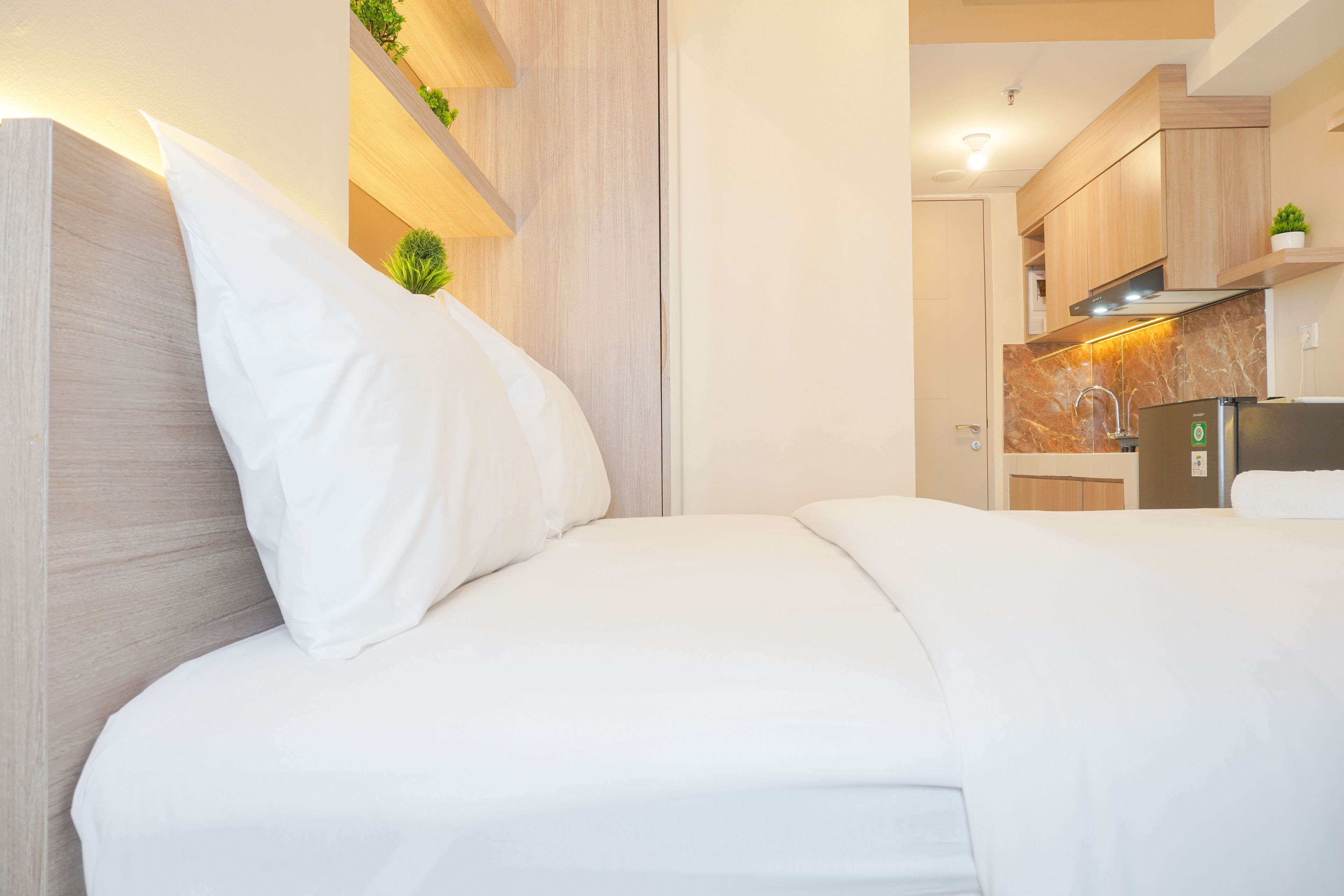 A modern bedroom with a wooden headboard, white bedding, and a small potted plant.