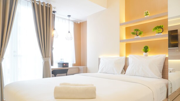 A hotel room with a large bed, a desk, and shelves with plants.