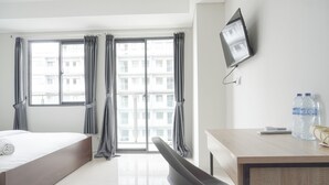 Habitación de hotel con cama, escritorio, silla, televisor y ventana con cortinas.