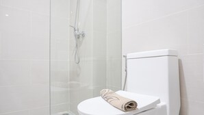 Un baño moderno con cabina de ducha de vidrio, un inodoro blanco y una toalla sobre el asiento.