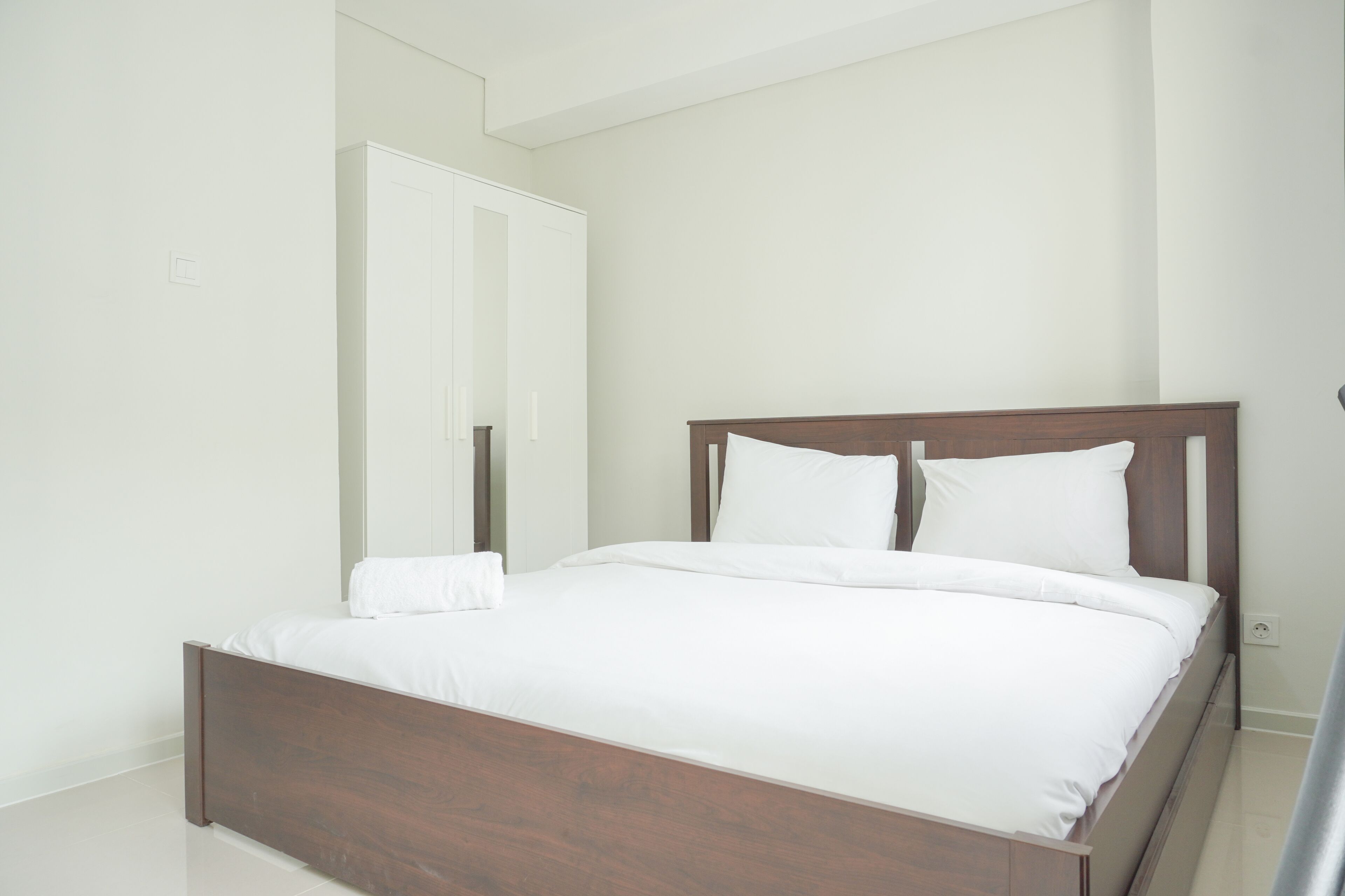 Ein Schlafzimmer mit einem hölzernen Bett, weißer Bettwäsche und einem weißen Kleiderschrank.
