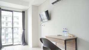 Una habitación de hotel moderna con un ventanal grande, un escritorio con silla, un televisor de pantalla plana montado en la pared y una botella de agua sobre el escritorio.