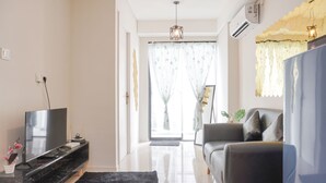 A modern living room with a flat-screen TV on a black TV stand, a grey sofa, and a black rug. - Nice And Comfort 2Br At Daan Mogot City Apartment (Jakarta)