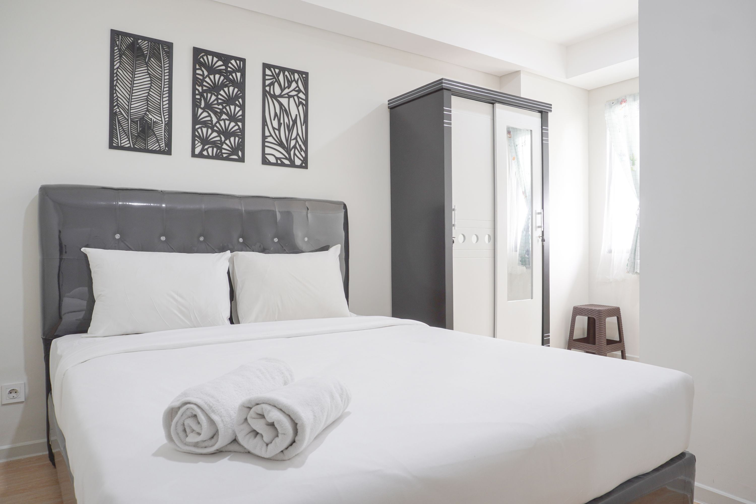 A neatly made bed with white linens and rolled towels, a grey upholstered headboard, and two abstract wall art pieces.