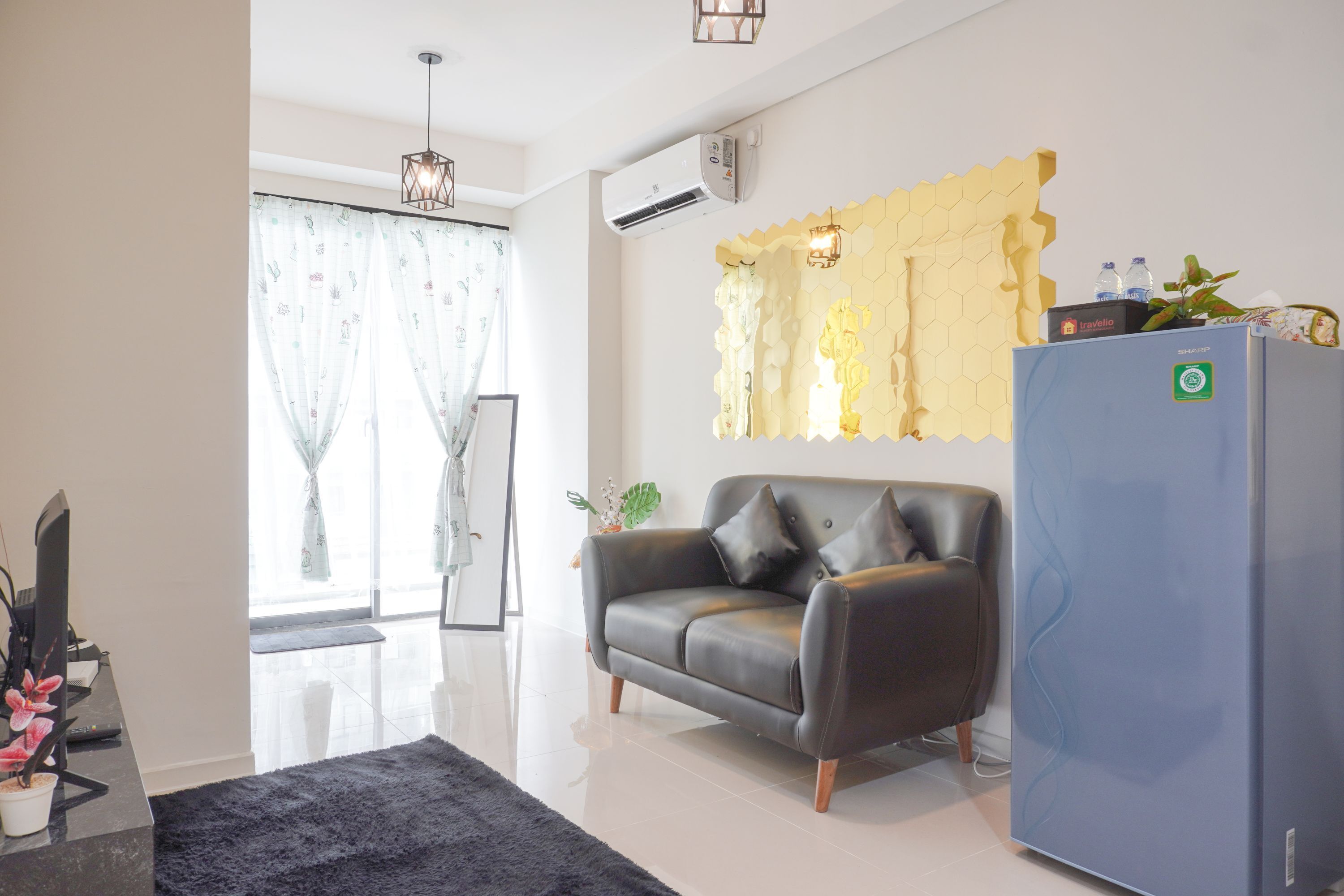 A modern living room with a sofa, a flat-screen TV, a refrigerator, and a window with curtains.