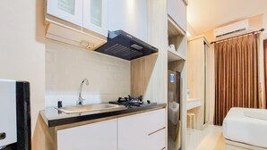 A compact kitchen with a sink, stove, and cabinets, leading to a small dining area with a white table and chairs. - Cozy Living Studio At Transpark Bintaro Apartment (South Tangerang)