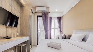 A hotel room with a bed, a desk with a flat-screen TV, and a window with curtains. - Cozy Living Studio At Transpark Bintaro Apartment (South Tangerang)