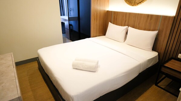 A neatly made bed with white linens and a folded white towel, a wooden headboard, and a bedside table with a lamp. - Aesthetic 2Br Connected To Mall At Supermall Mansion Apartment (Surabaya)