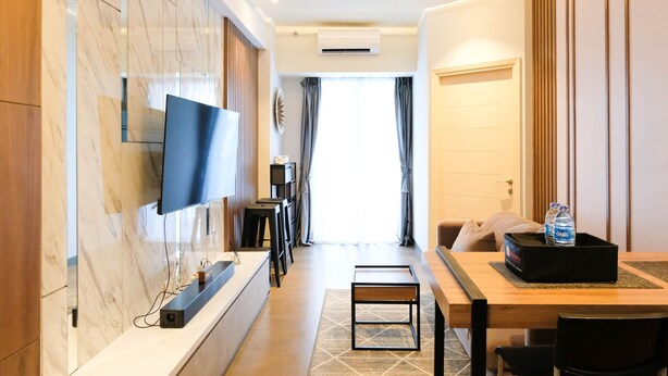 Ein modernes Hotelzimmer mit Wand-Fernseher, einem Holztisch mit Stühlen, einem kleinen Beistelltisch und einem Bett mit Kopfteil.