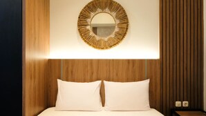 Ein Hotelzimmer mit einem hölzernen Kopfteil, einem runden Spiegel mit goldener Rahmung und zwei weißen Kissen.