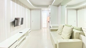 A modern living room with a white sofa, a flat-screen TV mounted on the wall, and a hallway leading to another room.