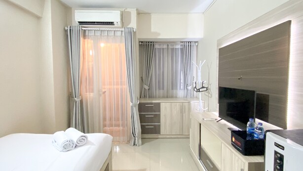 A hotel room with a bed, a desk with a flat-screen TV, an air conditioning unit, and a minibar. - Comfortable Studio Apartment For 1 Pax Grand Sentraland Karawang (Karawang)