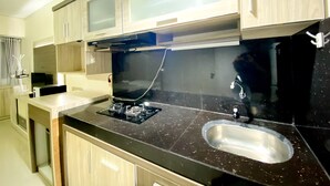 A modern kitchen with a black countertop, stainless steel sink, and wooden cabinets. - Comfortable Studio Apartment For 1 Pax Grand Sentraland Karawang (Karawang)