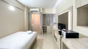 A compact hotel room with a single bed, a small kitchenette, a TV, and a window with curtains. - Comfortable Studio Apartment For 1 Pax Grand Sentraland Karawang (Karawang)