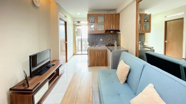 A modern living room with a flat-screen TV on a wooden stand, a light blue sofa with cushions, and a kitchen area with wooden cabinets and a tiled backsplash. - Nice 2Br Apartment At Gateway Ahmad Yani Cicadas (Bandung)