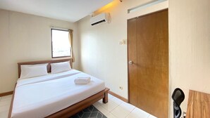 A hotel room with a bed, a window, an air conditioning unit, a wooden door, and a small table. - Nice 2Br Apartment At Gateway Ahmad Yani Cicadas (Bandung)