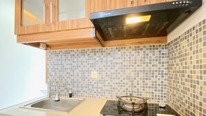 A modern kitchen with wooden cabinets, a black stove, and a tiled backsplash. - Nice 2Br Apartment At Gateway Ahmad Yani Cicadas (Bandung)