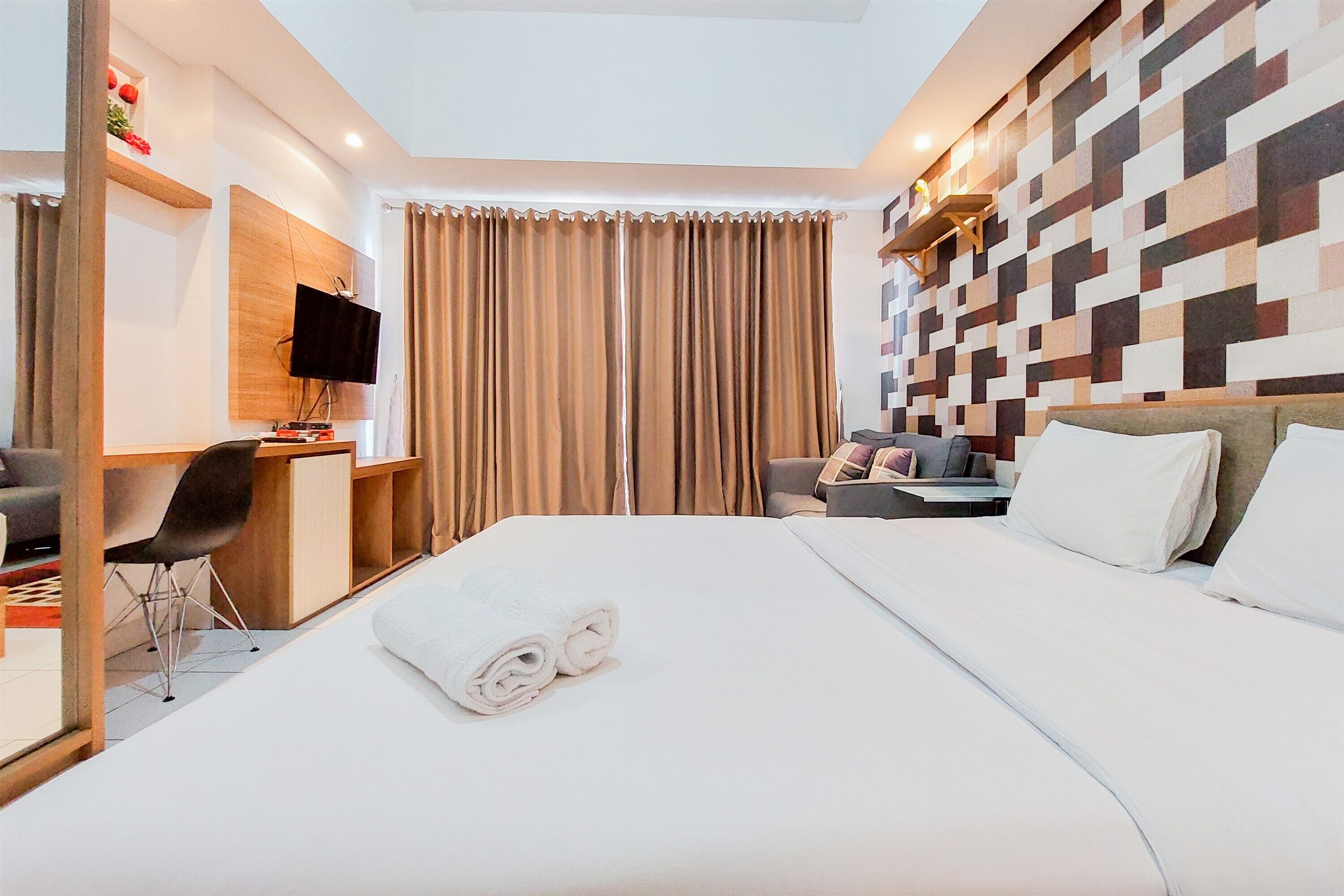 A hotel room with a bed, a desk with a chair, a television, and a wall with a geometric pattern.
