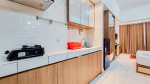 A modern kitchen with white tiles, wooden cabinets, a red sink, and a black appliance. - Warm And Homey Studio Room Casa De Parco Apartment (South Tangerang)